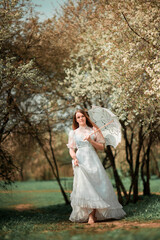 A girl in a park in a white dress and with an umbrella