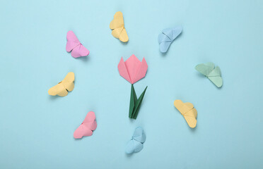 Origami butterflies flying in circle and tulip on blue background
