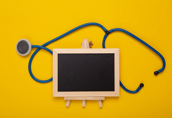 Mini Empty chalk board with copy space and stethoscope on yellow background. Medicine concept