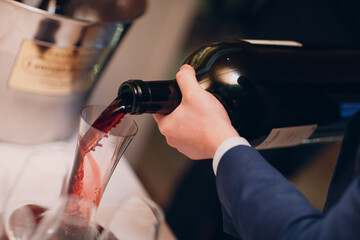 the waiter pours elite red wine into the decanter on the table in the restaurant