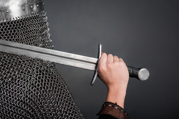 Back view of a knight in chain mail and a helmet with a sword on his shoulder on a dark background....