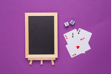 Mini blank chalk board with copy space and playing cards on purple background. Gambling concept