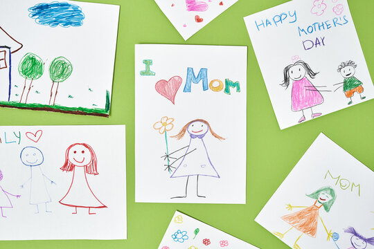 Top view of colorful child drawings with colored pencils for mothers day on green background, handmade greeting card for mom from child