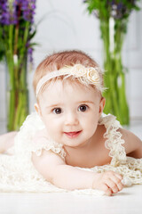 Portrait of a beautiful little baby girl with violet flowers. Sweet smiling girl lying on her stomach