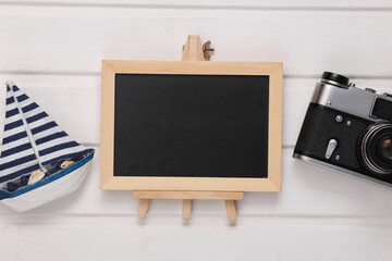 Travel composition of boat, camera and empty chalk board on white wooden background