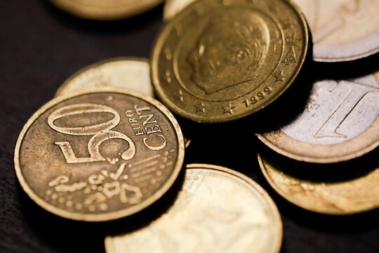 Shallow depth of field (selective focus) and macro image with a 50 Euro cents metal coin near other Euro coins on black background.