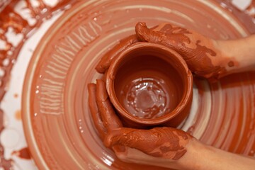 The hands of a master potter shape a clay jug that stands on a potter's wheel (Top view)