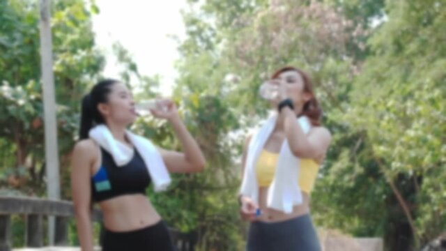 Footage shot with blur technique: Two Asian women taking a break from exercising in a park. And drink water from the bottle for refreshment