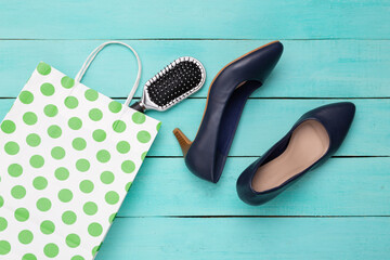 Paper polka dots shopping bag with shoes and hair brush on blue wooden background. Top view