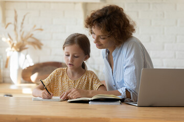 Private lesson. Attentive young woman tutor teacher help little girl pupil with studying math...