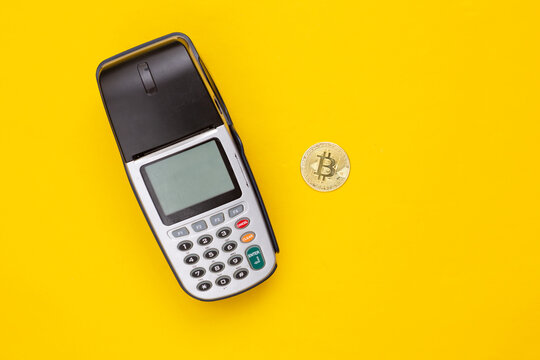 Payment terminal with bitcoin on yellow background. Top view