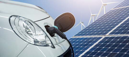 Close up of electric car with a connected charging cable on the background of solar panels and wind...