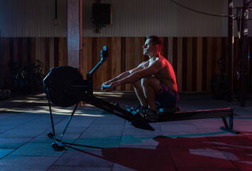 Muscular athletic man exercising in Simulation rowing exercise machine in red blue neon gradient...