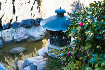 Naklejka premium Traditional Japanese lantern on a stone wall by a stream under camellia branches