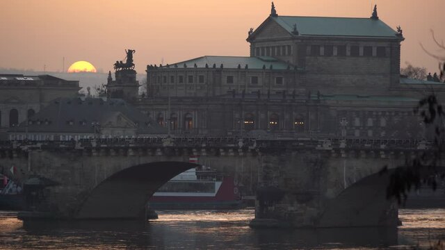 Sun is setting over the Augustus Bridge and Semperoper Opera Building in Dresden. Red sky glow due to suspended Sahara dust in the atmosphere