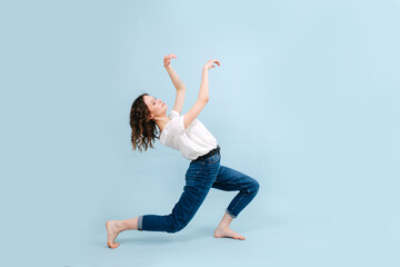 Funny contemporary dancer poses in front of blue studio background. Her legs in a lunge, arching herself back, making moves with her hands.