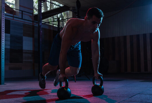 Muscular man push up with kettlebell in red-blue gradient light in dark cross fit hall