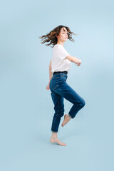 Dynamic contemporary dancer poses in front of blue studio background. She's bending knee with straightened ankle, like horse. In a body rotating motion.