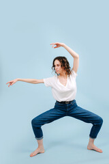 Fototapeta na wymiar Serious contemporary dancer poses in front of blue studio background. She's holding her hips spread in a line, knees at a right angle. Resembling traditional eastern martial art.
