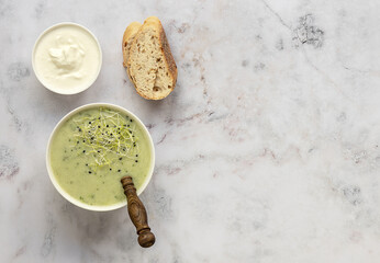 Broccoli cream soup served with cream and fresh bread on light marble table. Healthy vegetarian food concept. Top view, copy space
