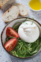 Close-up of salad with burrata cheese, cucumber and tomatoes, vertical shot on a beige stone surface