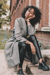 Portrait of an African American woman who sits on the steps near the building and poses