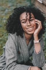 Portrait of an African American woman who holds her hand near her face and smiles