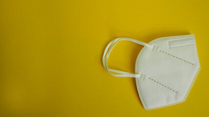 white anatomical medical mask lying on a yellow background top view . protection against coronavirus