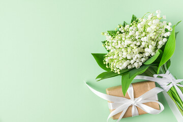 Spring lily of the valley flowers bouquet with gift box on pastel green background. Flat lay. Top view. Wedding concept