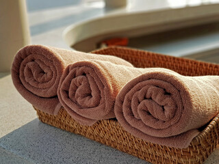 Rolled up brown bath towels in straw basket on counter outdoor.