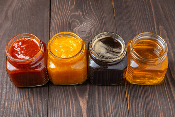 jars of peach and apricot jam and light and dark honey on a dark wooden background