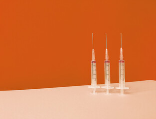 Three syringes on orange background with trendy skyline and copy space.