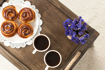 Two cups of coffee on a tray. A bun and a bouquet of flowers. Breakfast in bed.