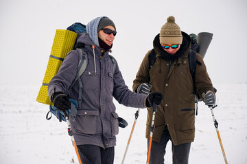 Fototapeta na wymiar The guys talk during the winter expedition. They are wearing warm jackets, hats and large backpacks. They stand in the snow and hold trekking sticks