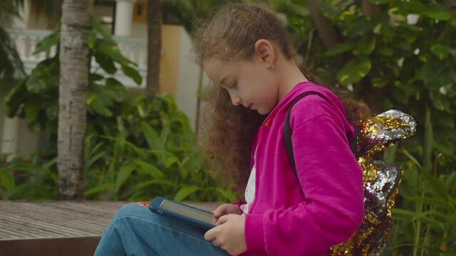 Cute child using a digital tablet technology device telephone or laptop. Children tech addiction concept play game. Plays in the phone sitting on street alone.