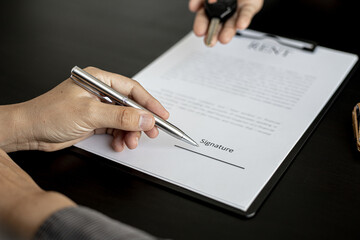 The renter is signing a car rental agreement with the car rental company. After discussing the details and charges with the employee, the employee hand over the car keys to the renter.