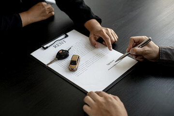 A car rental company employee pointed out the renter to sign the rental agreement after discussing the details and rental terms with the renter. Concept of car rental.
