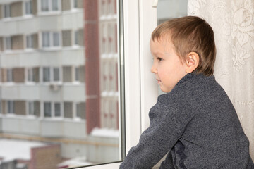 A 6-year--old  boy is bored and looks out the window from his apartment