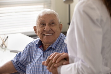 Close up smiling mature man and female caregiver wearing white uniform holding hands, doctor nurse...