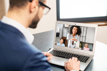 Bearded businessman in glasses and formal wear using app for distance video communication with coworkers, networking, meeting online in pandemic, looking at the laptop screen with people profiles