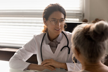 Close up smiling female doctor physician wearing glasses consulting mature patient during appointment in hospital, listening complaints, discussing medical checkup results, health insurance concept