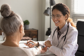 Close up smiling female doctor wearing glasses checking old woman blood pressure at meeting in...