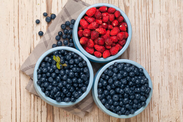 Bilberry and strawberry in blue bowls on white vintage wooden background, top view food composition