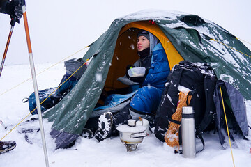 The guy in the tent eats porridge from a plate during winter travel © Serhii Prystupa