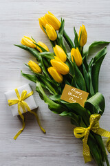 Bouquet of tulips with gift box on white wooden background. Craft greeting card with happy Women's Day. Top view, flat lay.