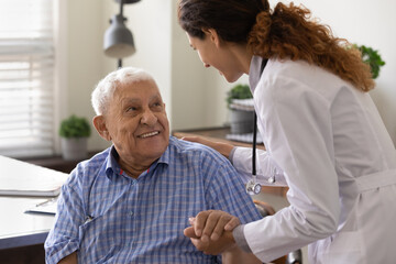 Close up caring nurse holding smiling mature patient hand at meeting in hospital, doctor caregiver...