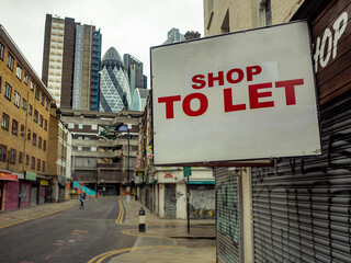 Shop To Let sign on empty street of closed retail shops with London city in the background