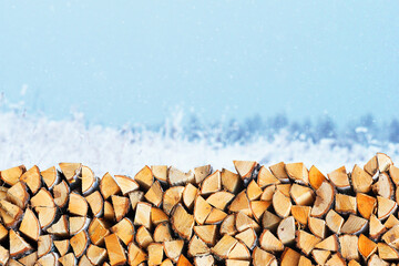 Woodpile of firewood on the background of a winter landscape. Firewood stack, village