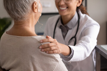Close up back view smiling female doctor wearing uniform touching mature patient shoulder, expressing empathy and care, successful treatment or medical checkup result, psychological help concept