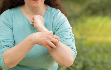 Close-up of woman scratching arm because it stings in a park with a green background